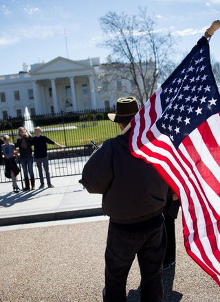 Mann mit US-Flagge steht vor Weißem Haus.; Rechte: dpa