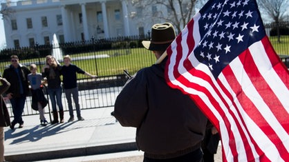 Ein Mann steht mit US-Flagge vor Weißem Haus.