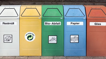 Fünf verschiedenfarbige Müllcontainer stehen nebeneinander.