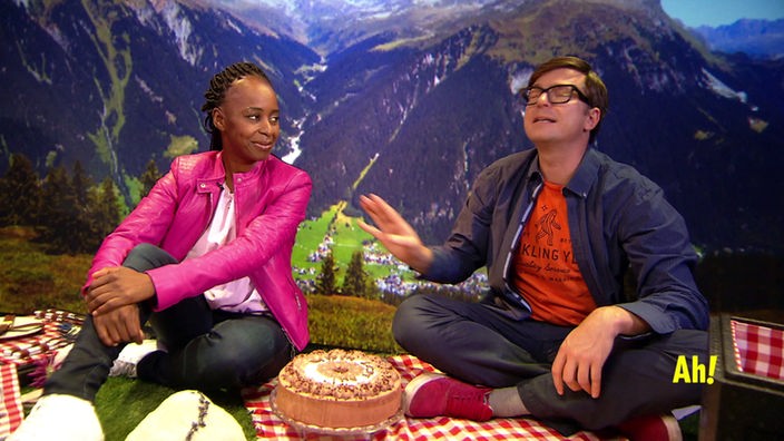 Shary und Ralph sitzen auf einer Picknickdecke, vor ihnen steht ein Kuchen