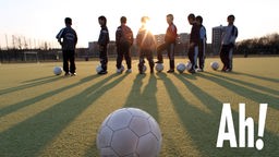 Kinder auf einem Fußballplatz im Sonnenuntergang mit Ball im Vordergrund