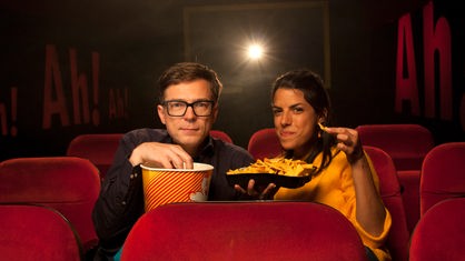Clarissa und Ralph sitzen in roten Kinosesseln und halten Popcorn und Nachos in den Händen.